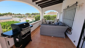 Een balkon met een barbecue, buitenmeubels en uitzicht op de omgeving.