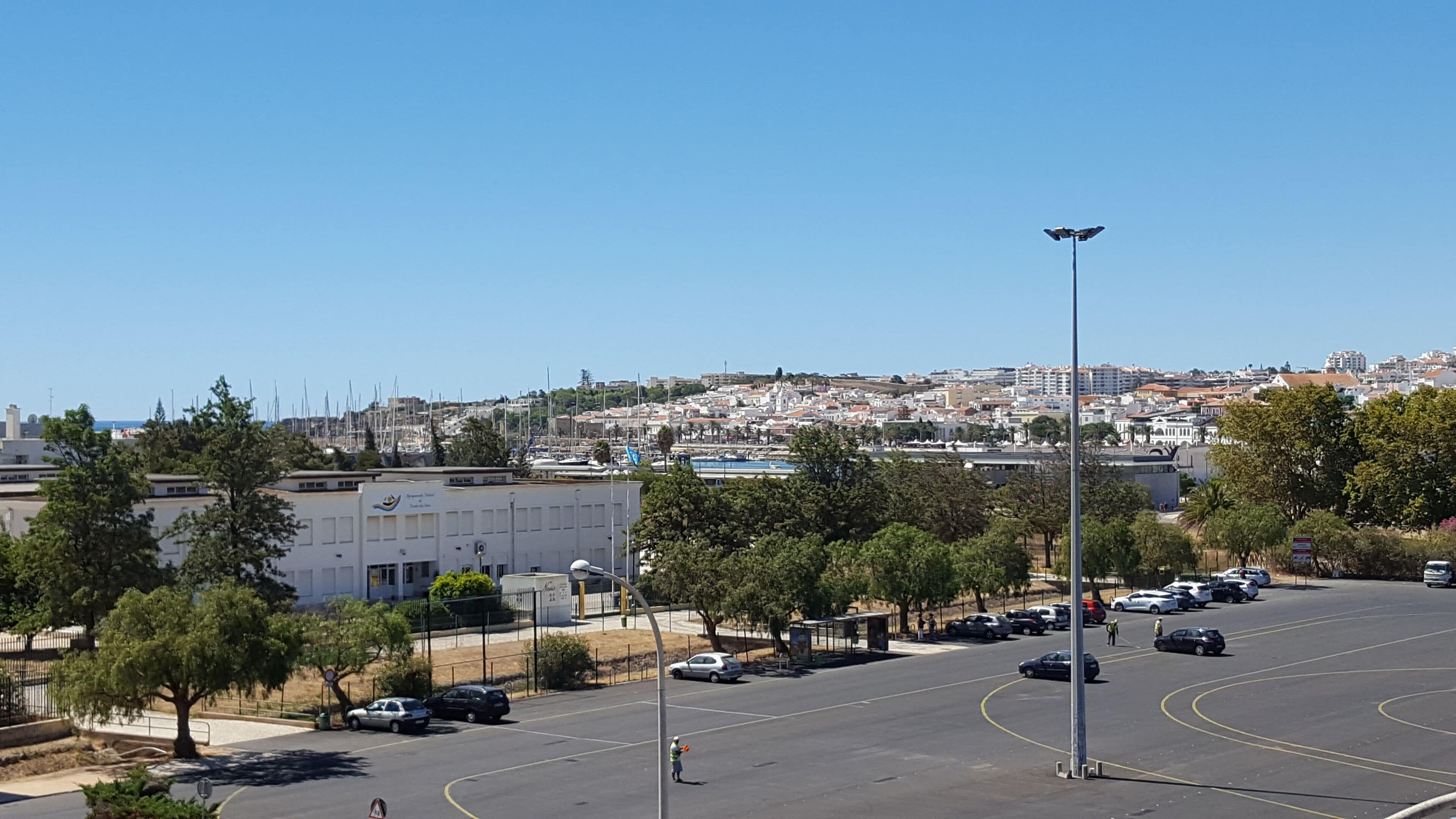 A parking lot with cars, a building with a sign, and a view of a town in the background.