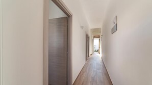 Un couloir au sol en bois et aux murs blancs, qui mène à une porte au fond.