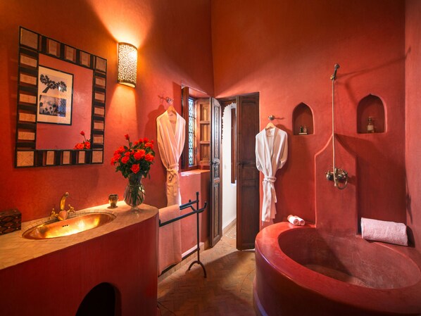 Une salle de bain avec une grande baignoire rouge, un lavabo orné d’un vase rempli de fleurs rouges et un miroir avec un cadre.