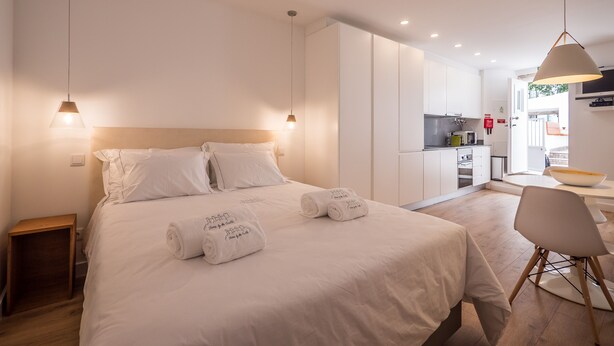 Una camera d'albergo moderna con un letto grande, un comodino, una sedia e un angolo cottura sullo sfondo.