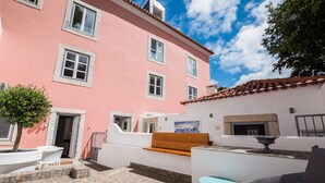 Un edificio rosa con rifiniture bianche, un patio piastrellato, una panchina e un tavolo.