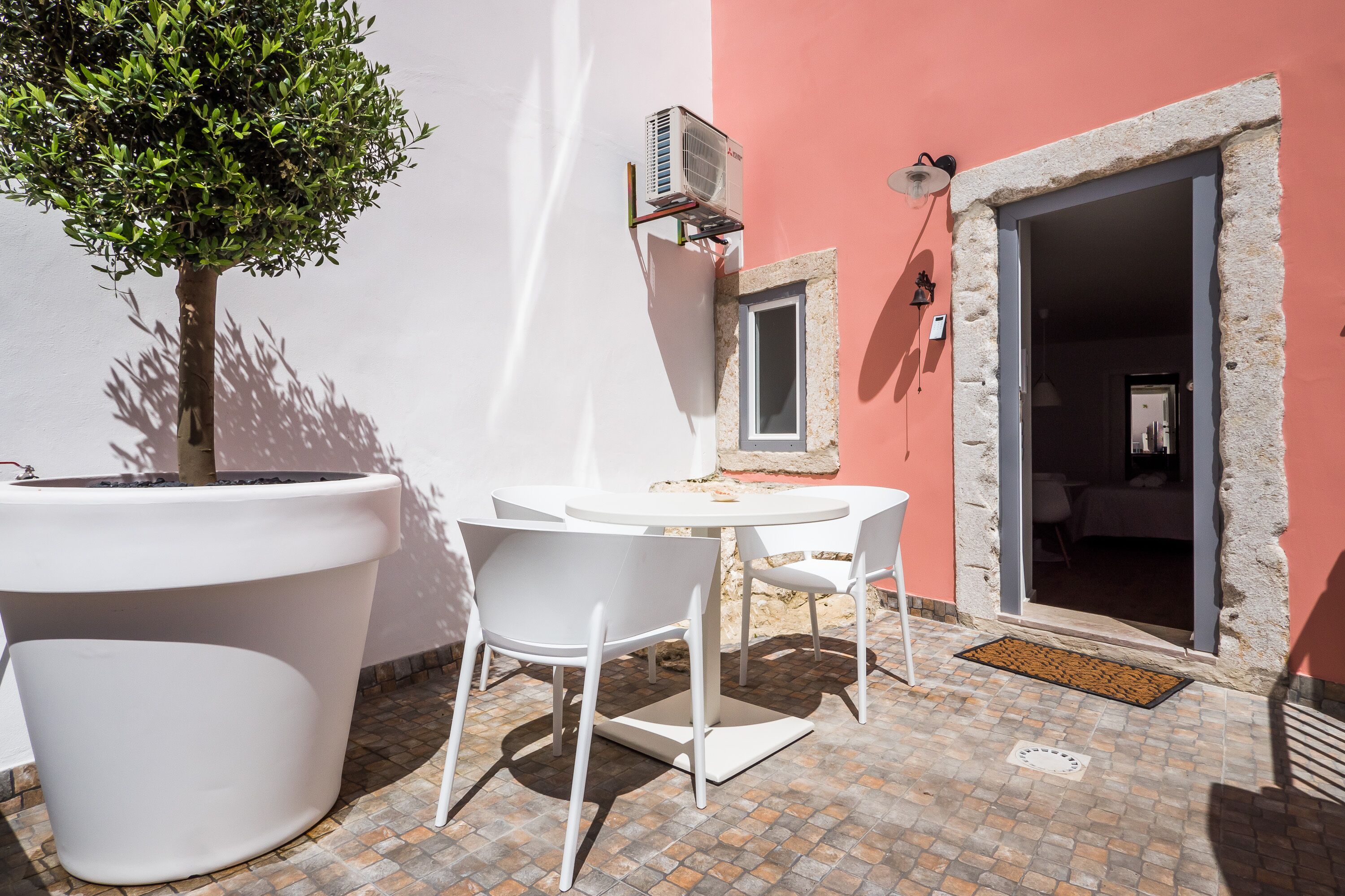 Un petit espace extérieur aménagé avec une table et des chaises, un pot de fleurs et une porte donnant sur une pièce.
