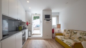 Una cucina moderna con mobili bianchi e un piano di lavoro grigio, un divano giallo con motivo floreale e un televisore montato a parete.