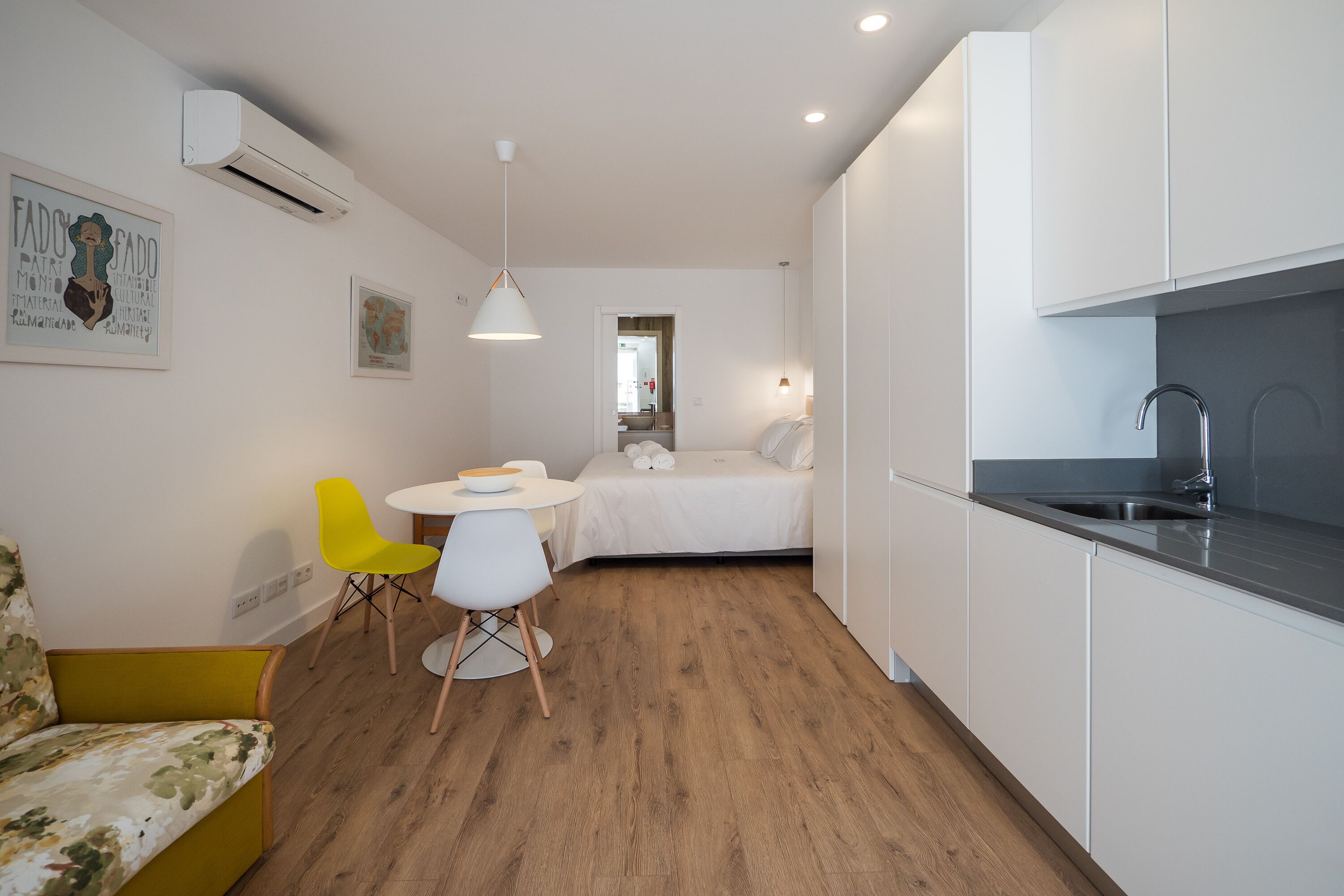 A compact room with a bed, a small dining area, a kitchen with a sink, and a yellow chair.