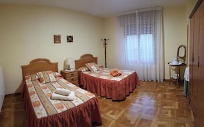 Une chambre avec deux lits, un plancher en bois, une fenêtre avec des rideaux, un porte-manteau et un miroir au mur.