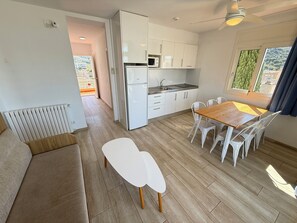 A modern kitchen with white cabinets, a dining area with a wooden table and white chairs, and a view of greenery outside.