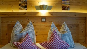 Interior de una cabaña de madera con una cama, almohadones a cuadros y obras de arte colgadas en la pared.