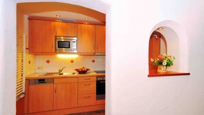 Una cocina compacta con armarios de madera, un microondas integrado y una pequeña ventana con un jarrón de flores.