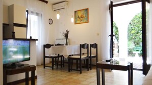 Uma sala de jantar com uma mesa posta para quatro pessoas, uma televisão em um suporte e um quadro na parede.