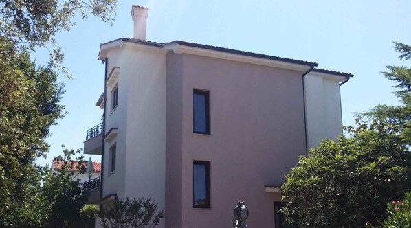 A two-story building with a flat roof, a chimney, and a balcony on the upper floor.