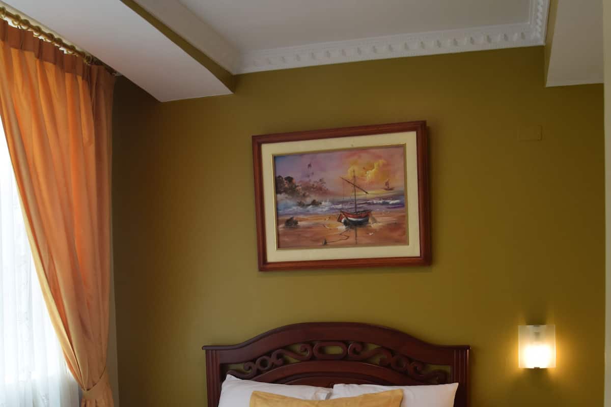 Ein ordentlich gemachtes Bett mit einem Laptop, einem Bild an der Wand und einer Nachttischlampe.