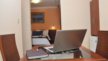 Ett hotellrum med en säng, ett skrivbord med en bärbar dator, ett anteckningsblock och en penna. Det finns en tavla på väggen och ett litet bord med en lampa.