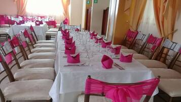 Una larga mesa de comedor dispuesta con servilletas rosas, cubiertos y copas de vino, rodeada de sillas adornadas con cintas rosas.