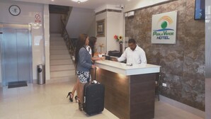 A hotel reception desk with a receptionist, a guest with a suitcase, and a staircase in the background. - Hotel Perla Verde (Esmeraldas)