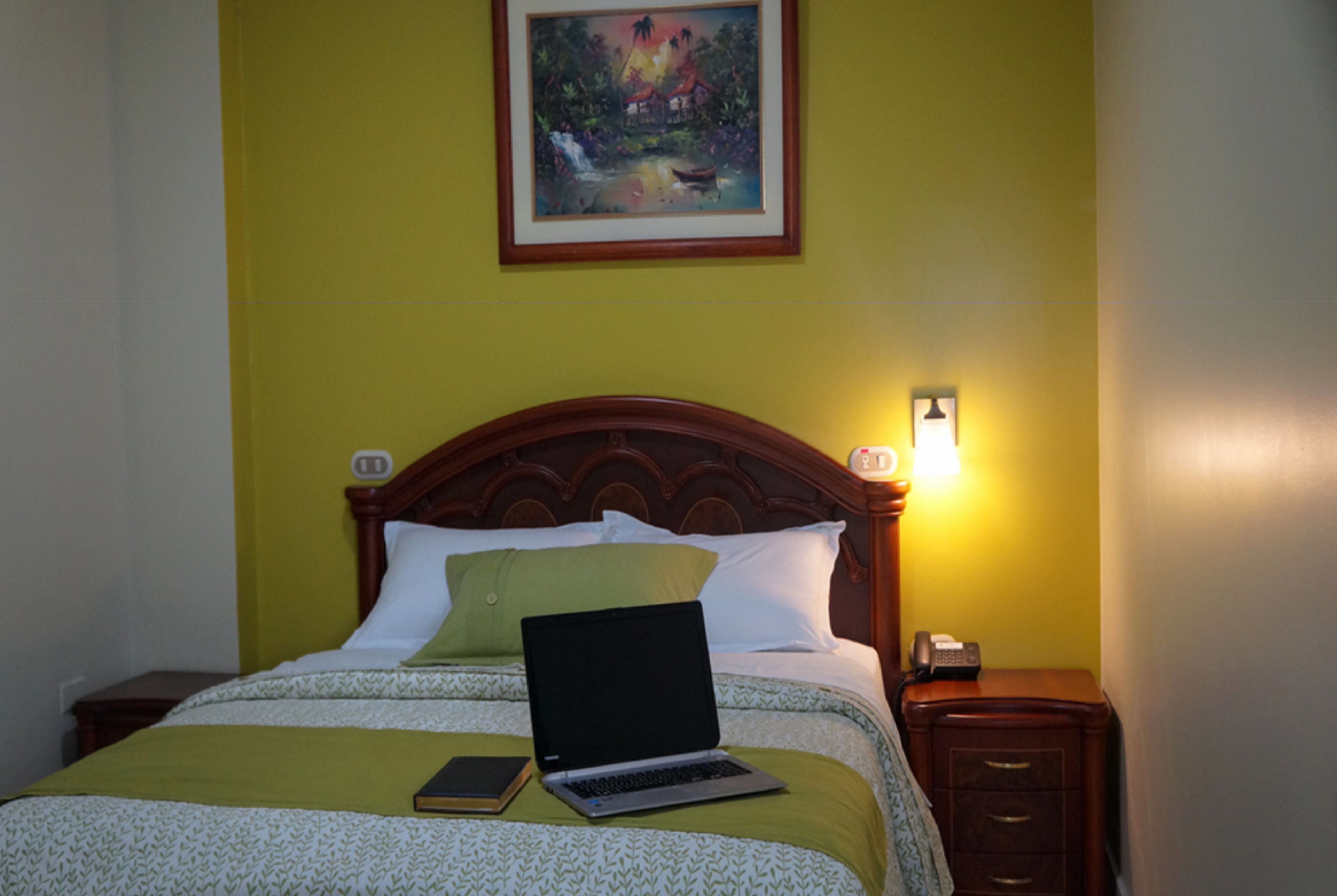 A bed with a laptop, a book, and a bedside table with a lamp.