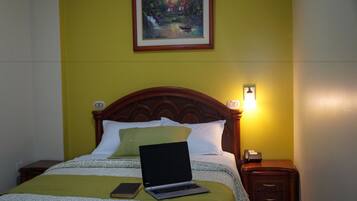A bed with a laptop, a book, and a bedside table with a lamp.