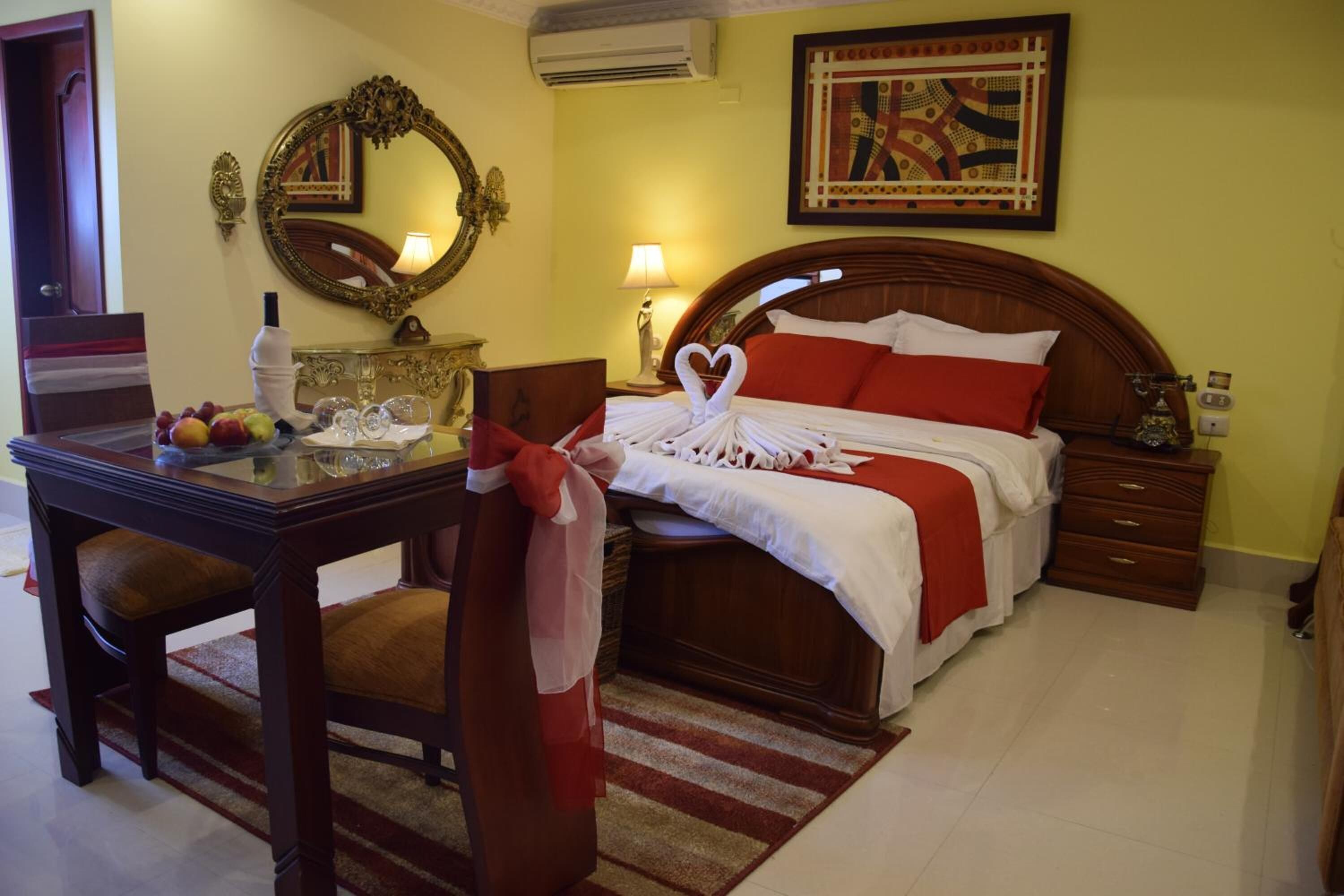 Habitación de hotel con cama de madera, una mesita de noche con lámpara, espejo y frutero.