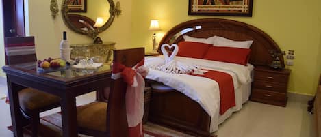 Habitación de hotel con cama de madera, una mesita de noche con lámpara, espejo y frutero.