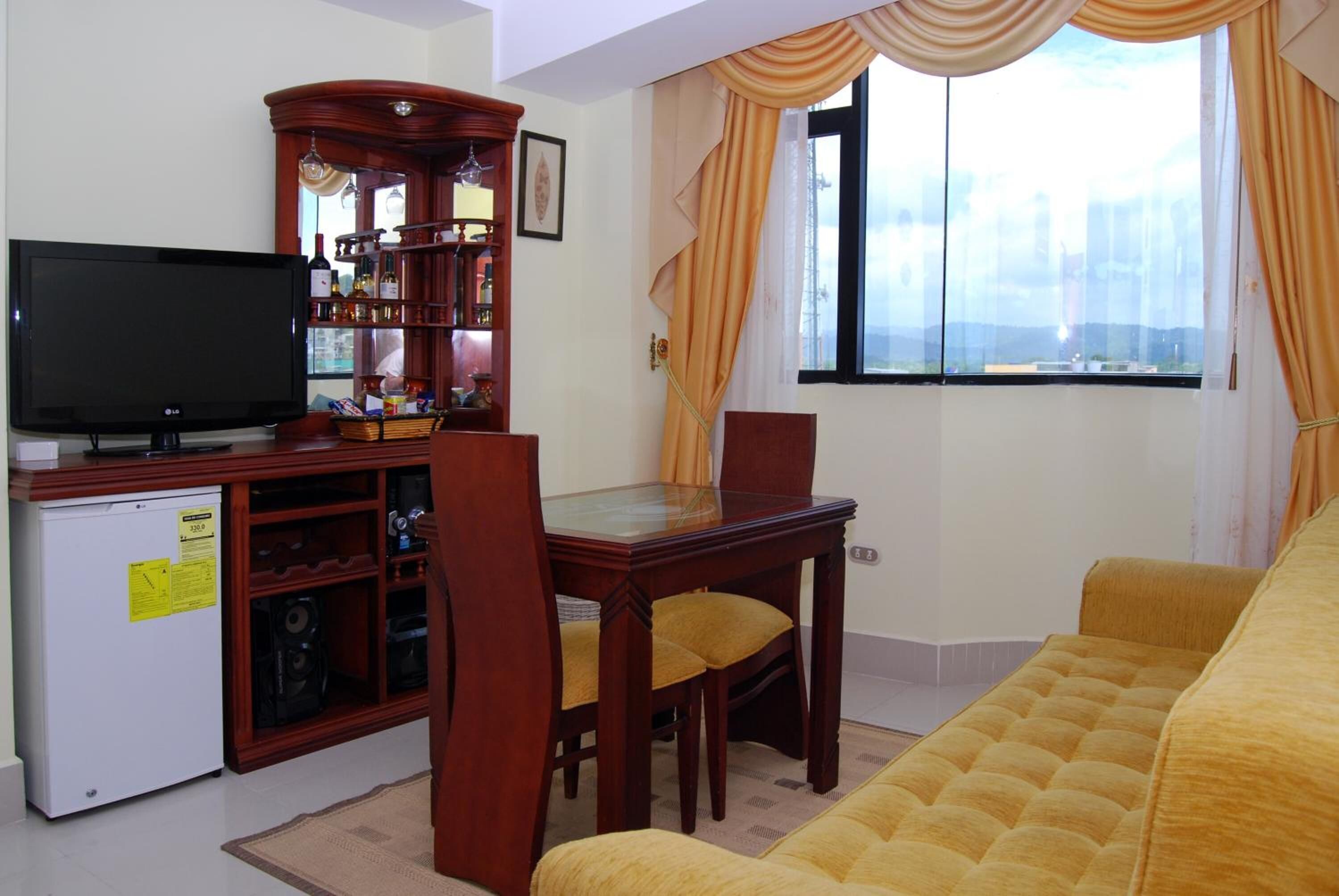 Una sala de estar con televisor, un mueble de madera con estantes, una mesa de comedor con sillas y un sofá.