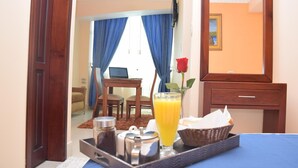 A hotel room with a bed, a breakfast tray with a glass of orange juice, a rose, and a TV on the wall. - Hotel Perla Verde (Esmeraldas)