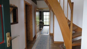 A wooden staircase leading to a second floor, a hallway with a patterned rug, and a view of a room with a window and a chair. - Vacation home Hanse in the vacation village Altes Land - Holiday home 327 Hanse 80sqm for max. 7 persons (Hollern-Twielenfleth)