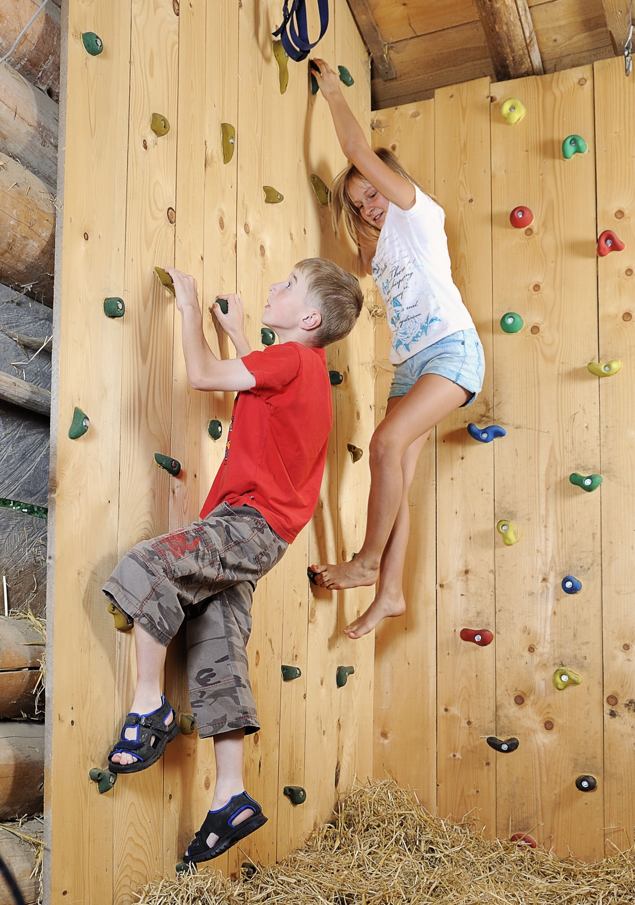 Two children climbing a wooden wall with colorful holds.