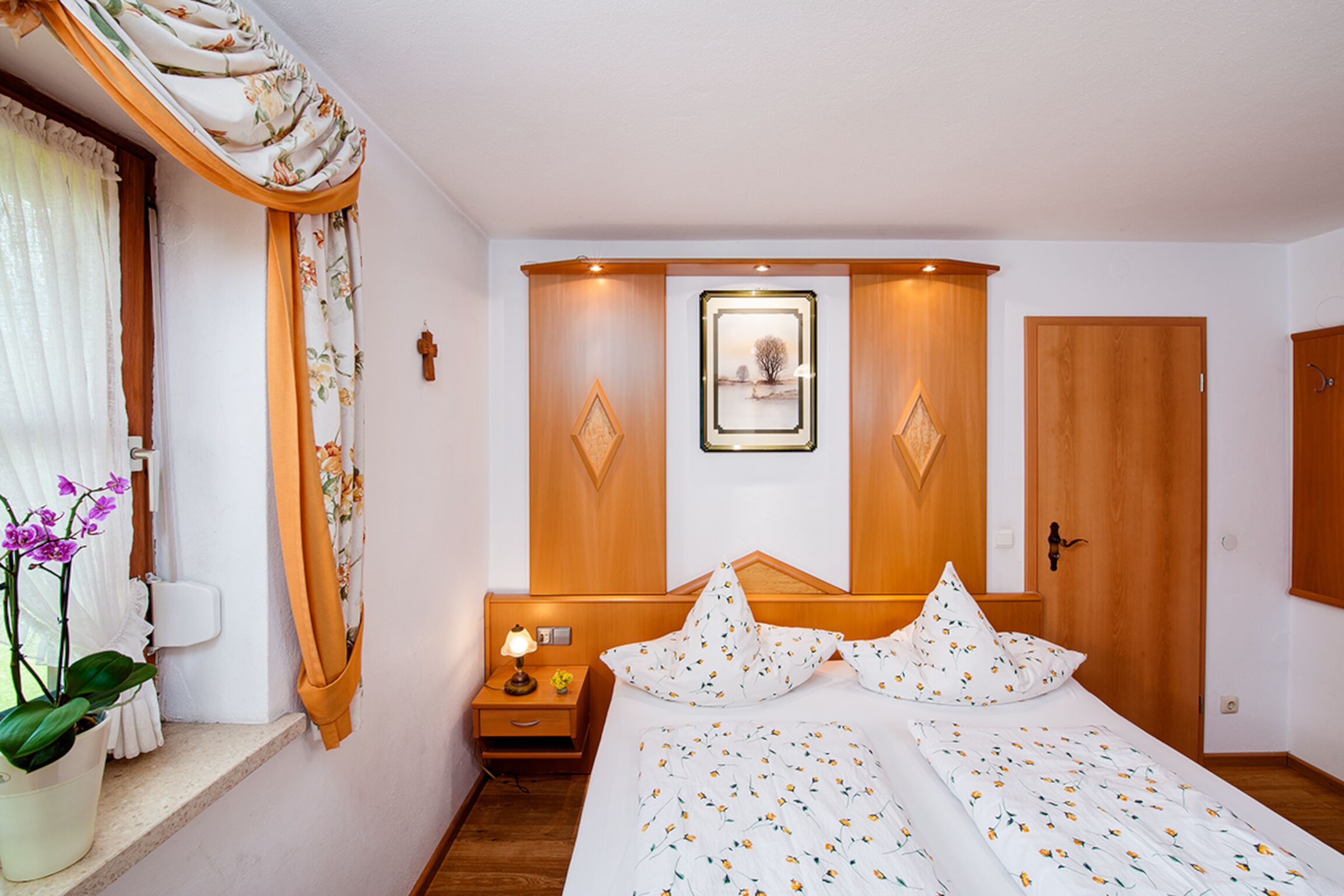 A bedroom with a bed, a nightstand, a potted plant, and a window with curtains.