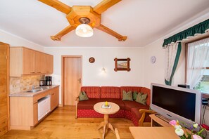 En kompakt opholdsstue med tekøkken, sofa, fjernsyn og spiseplads.