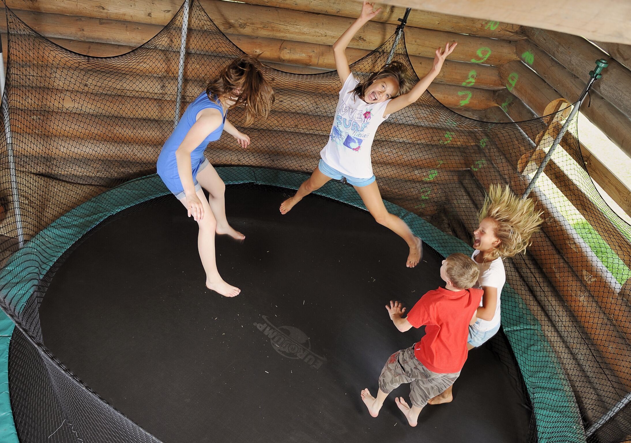 Un trampoline doté d’un filet de protection, entouré de murs en bois et muni d’un sol vert.
