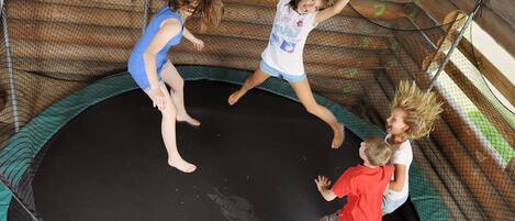 Un trampoline doté d’un filet de protection, entouré de murs en bois et muni d’un sol vert.