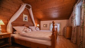 Une pièce en bois avec un lit, une table de chevet, une lampe et une fenêtre ornée de rideaux à motifs floraux.