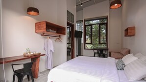 Un dormitorio con una cama grande, un escritorio de madera, una silla, un televisor y una ventana con vistas a árboles.