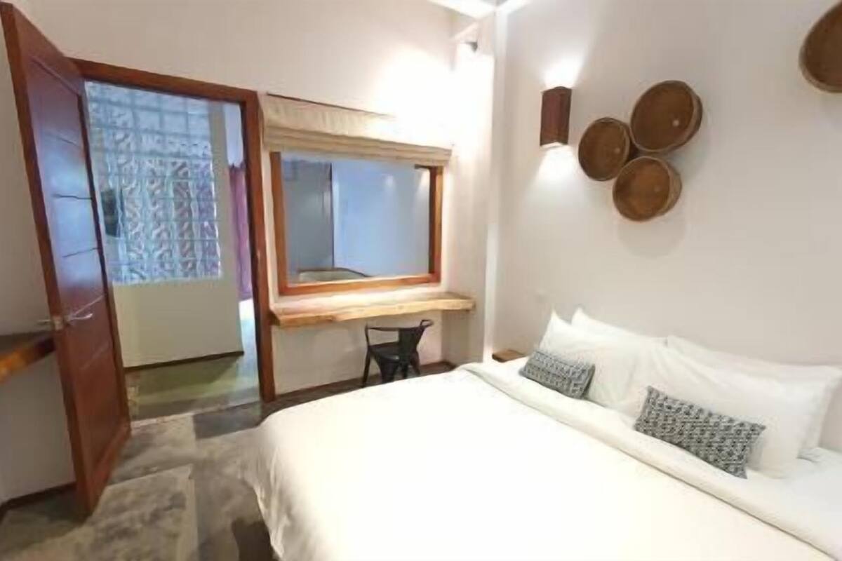 Ein Schlafzimmer mit Bett, Schreibtisch, Stuhl, Fenster und Tür.