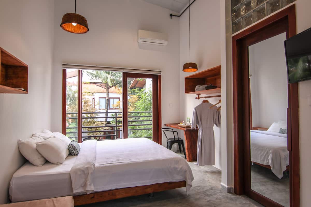 Ein Schlafzimmer mit einem großen Bett, einem Schreibtisch und einem Stuhl. Ein Fenster bietet Blick auf Grünflächen und ein Gebäude.