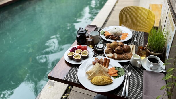 Una mesa de comedor con diversos alimentos y bebidas, ubicada junto a una piscina.