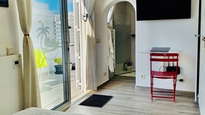 Une chambre d’hôtel avec un lit, un téléviseur fixé au mur, un fauteuil rouge et une vue sur l’extérieur par une porte vitrée.