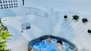Un bain à remous où se trouvent deux personnes, entouré d’une terrasse carrelée agrémentée de plantes en pot.