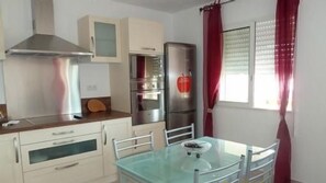 Una kitchenette con extractor de acero inoxidable, horno empotrado, refrigerador y una mesa de vidrio con sillas.