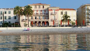 Ein Hotel am Wasser mit Balkonen, Sitzgelegenheiten im Freien und Palmen.