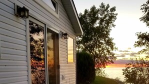 A house with a porch, two blue Adirondack chairs, and a view of the sunset over the water.