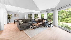 A spacious living room with a sectional sofa, a coffee table, and a dining area with a table and chairs. Large windows offer views of greenery outside. - 3BR/2BA Spinnaker! Close to Beaches! Pet Friendly! Amenity access included! (Seabrook Island)