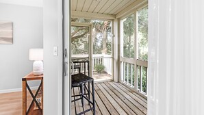 A wooden deck with a table and chair, a white door leading to an outdoor area with a view of trees. - 3BR/2BA Spinnaker! Close to Beaches! Pet Friendly! Amenity access included! (Seabrook Island)