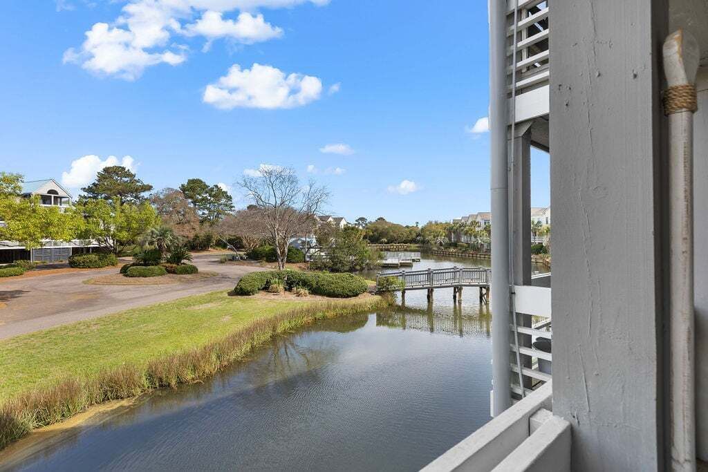 Una vista di un fiume tranquillo con un ponte di legno, circondato da vegetazione e edifici residenziali.
