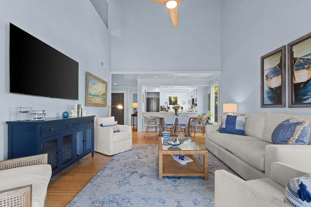 A spacious living room with a large flat-screen TV, a dining area with a table and chairs, and a kitchen in the background.