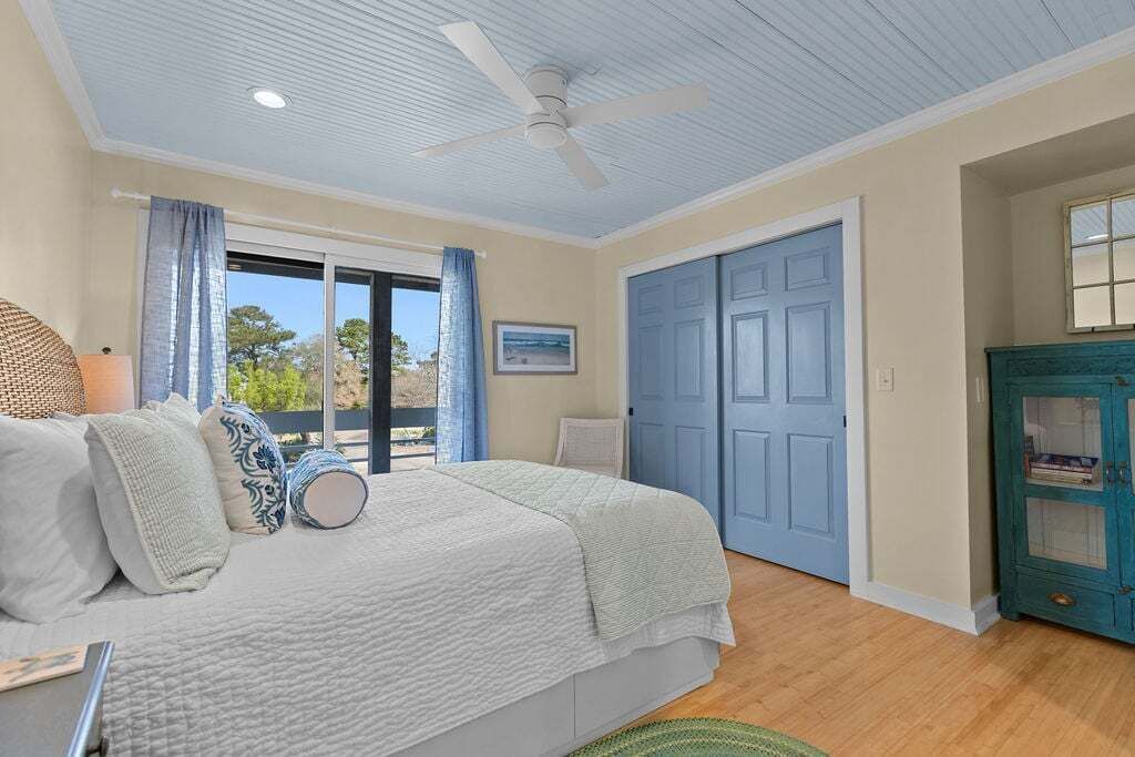 A bedroom with a bed, a ceiling fan, a door, and a window with curtains.
