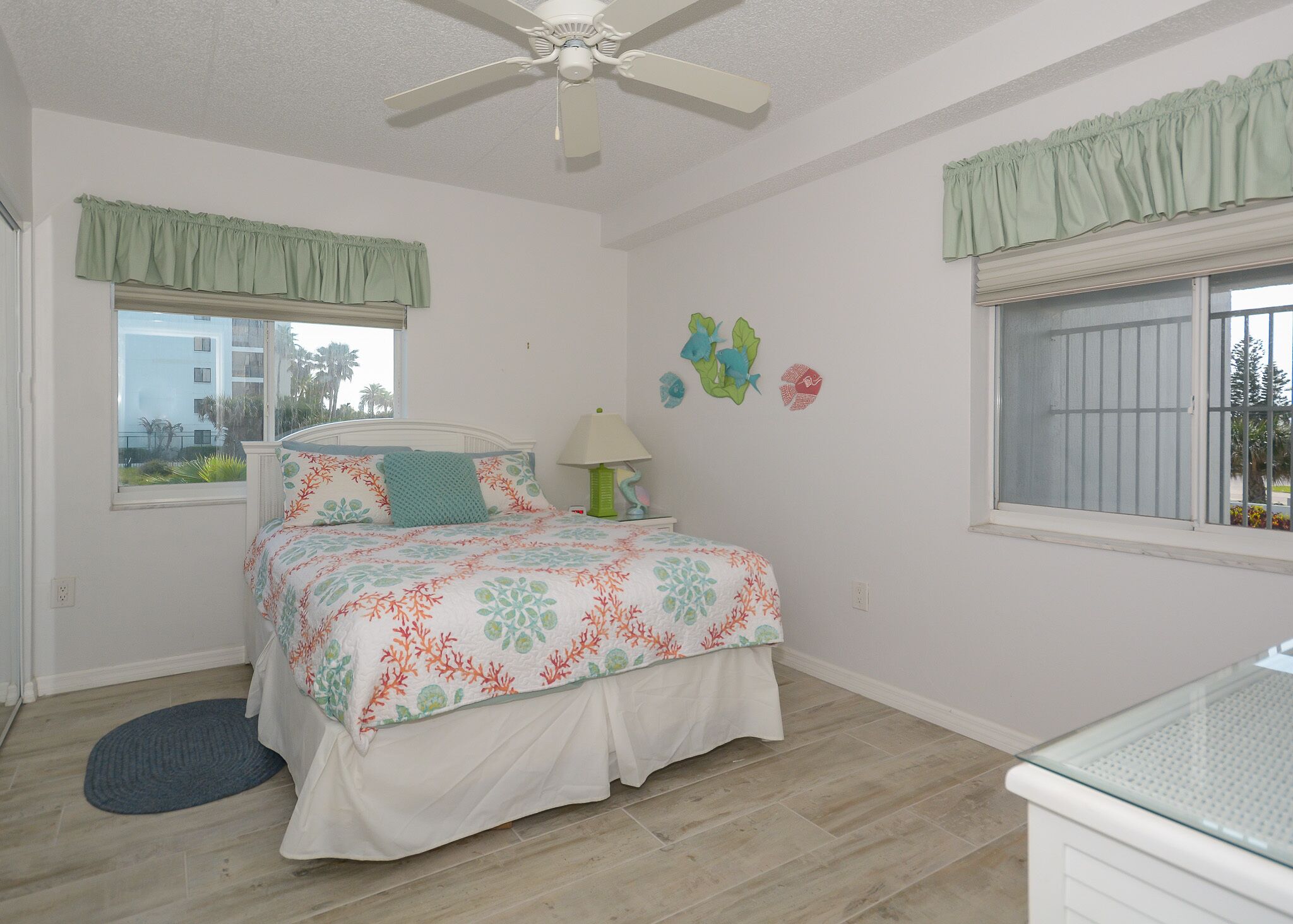 A bedroom with a bed, a ceiling fan, a window with a view, and a wall with decorative stickers.