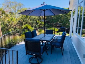 A deck with a table and chairs, a blue umbrella, and a view of greenery. - Spectacular Marsh Views! Walk to North Beach!  Sleeps 8! Amenity Access included! (Seabrook Island)