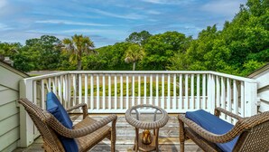 Una terraza de madera con mobiliario de mimbre y barandilla blanca.
