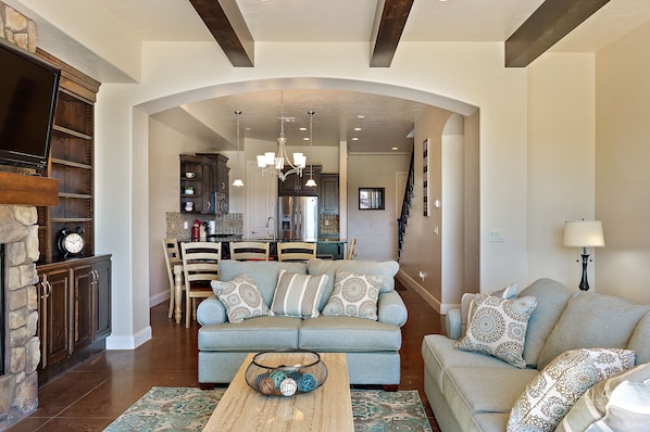 A living room with a sofa, coffee table, and fireplace. There is a kitchen in the background with cabinets and a dining area. - Above Par GOLF COURSE VIEWS!! 2 Community Pools! (Washington)